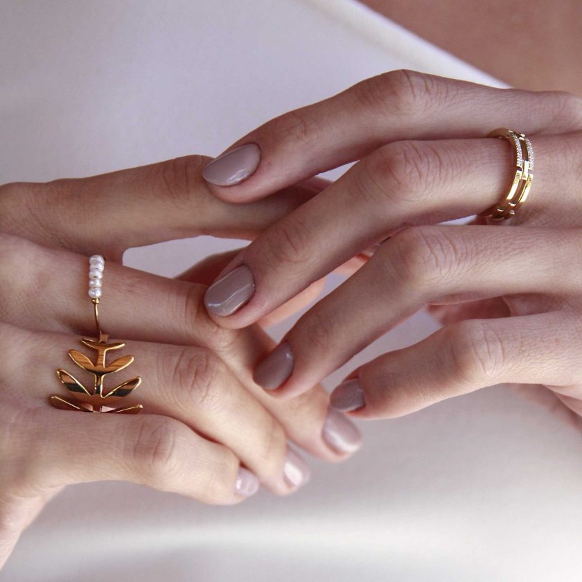 manos de mujer con anillo fino con detalle de cinco perlas naturales pequeña en el frente y anillo de hoja dorado